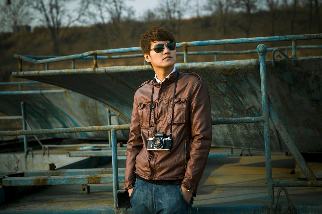 Man Wearing Brown Leather Jacket With Black Dslr Camera Standing on Skate Park Selective-focus Photography