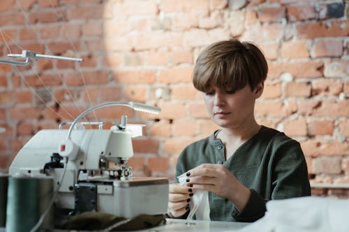 Free Man in Green and Black Stripe Sweater Using White and Gray Sewing Machine Stock Photo