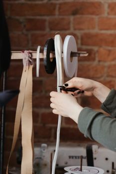 A close-up of hands working with ribbons on a stand against a brick wall backdrop in a craft setting.