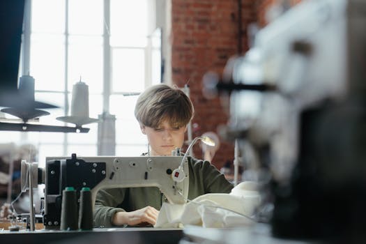Young seamstress concentrating on sewing in a well-lit workshop with industrial sewing machines.