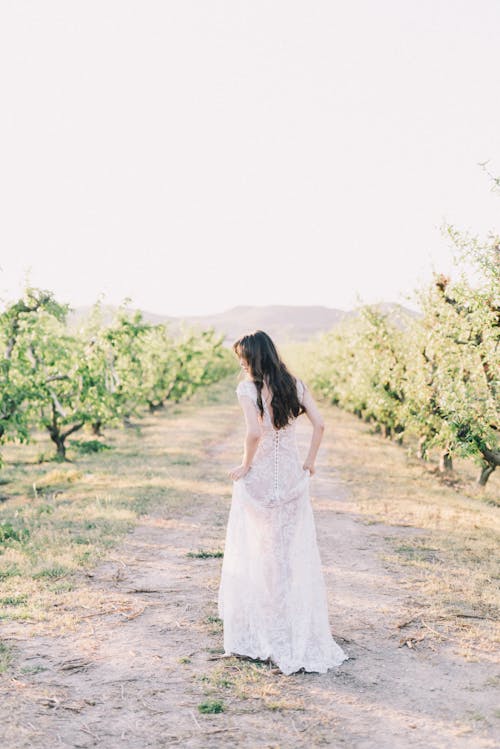 A Woman in White Dress Walking on Dirt Road