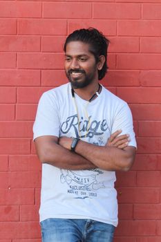 A cheerful man with a beard stands casually against a red brick wall, exuding confidence.