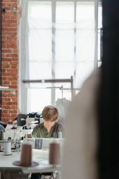 A dedicated seamstress works diligently in a bustling sewing workshop, surrounded by equipment.