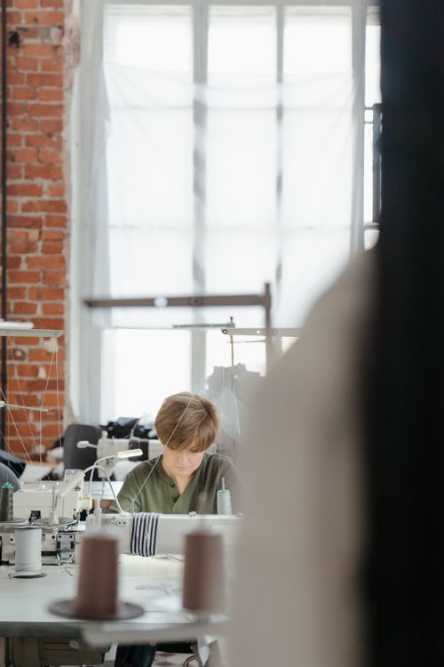 Free A dedicated seamstress works diligently in a bustling sewing workshop, surrounded by equipment. Stock Photo