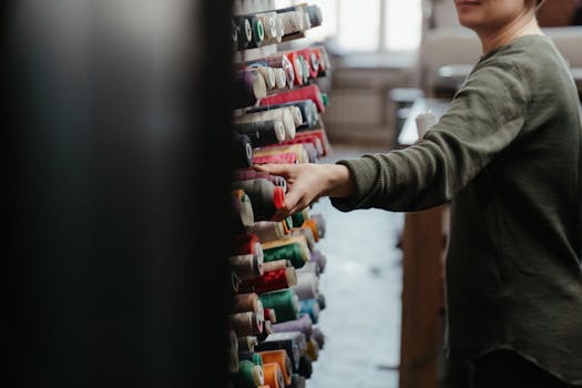 Person choosing colorful sewing thread spools from organized rack in workshop.