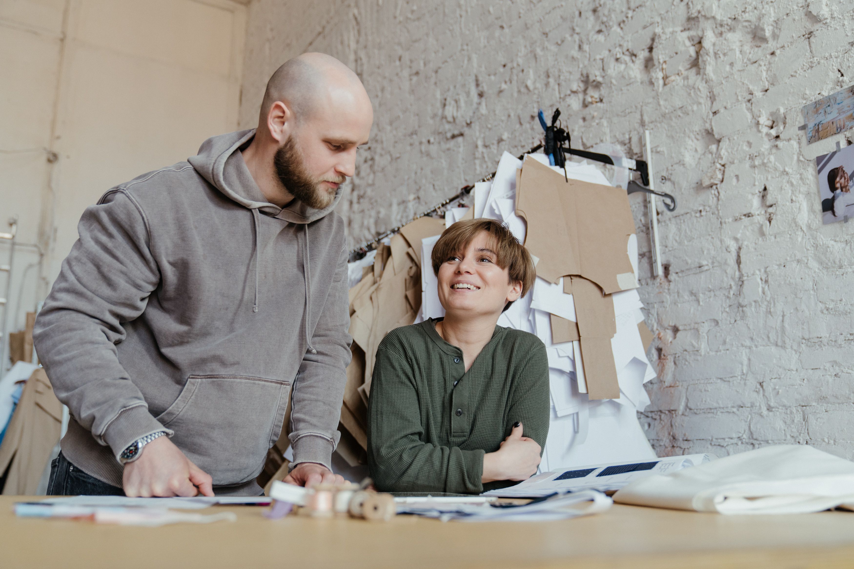 Two fashion designers collaborating in a trendy workshop with patterns and sketches.