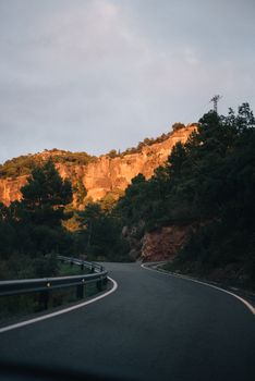 黄金时段，一条宁静的弯曲道路穿过充满生机的绿色森林与岩石悬崖