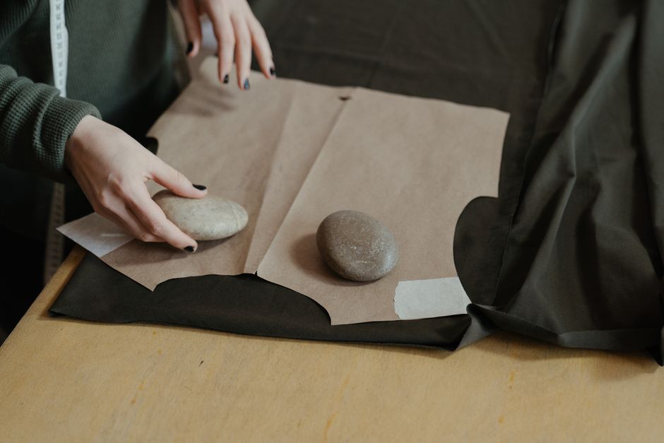A dressmaker uses paper patterns and rocks to craft a piece of clothing in a workshop.
