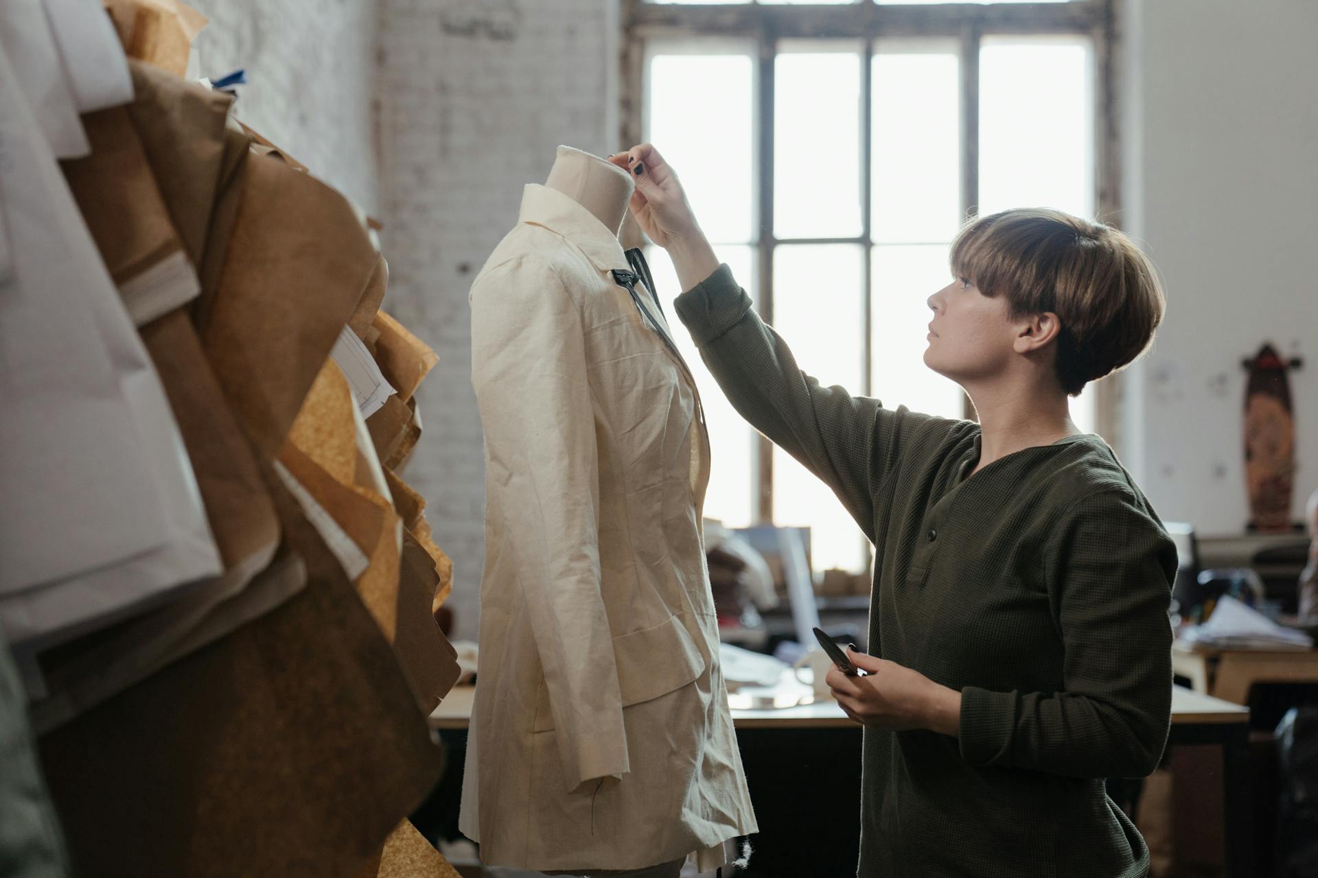 A tailor makes adjustments to a garment on a mannequin in a bright workshop.