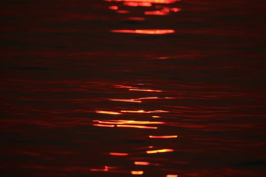 Vivid sunset reflecting from uneven surface of red wavy sea in sunlight at dusk