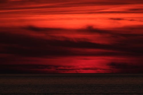 Vibrant red evening sky covered with dense clouds above dark silent endless sea