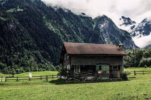 Free Picturesque scenery of old rustic cottage surrounded by coniferous high cloudy mountains and green valley Stock Photo