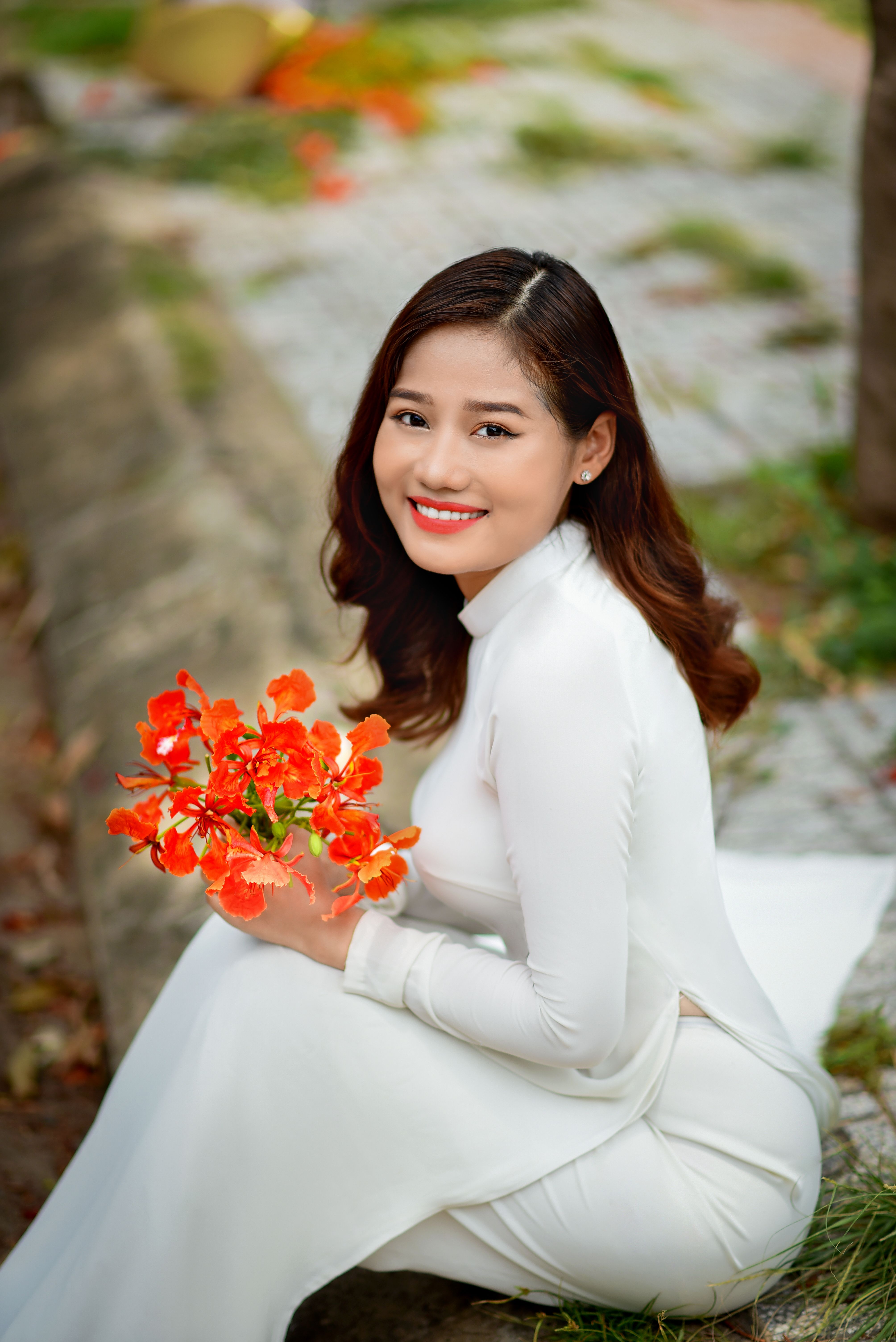 Beautiful woman in white Ao Dai holding vibrant flowers outdoors in Vietnam.
