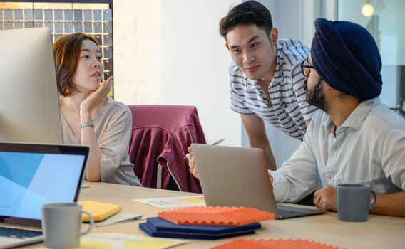 Three professionals engage in a collaborative discussion using laptops in a modern office.