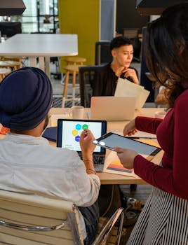 Young professionals discussing a project in a contemporary office setting with laptops and tablets.