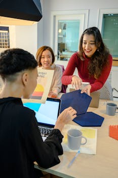Three colleagues discussing ideas around a desk with laptops, showcasing teamwork in a modern office environment.