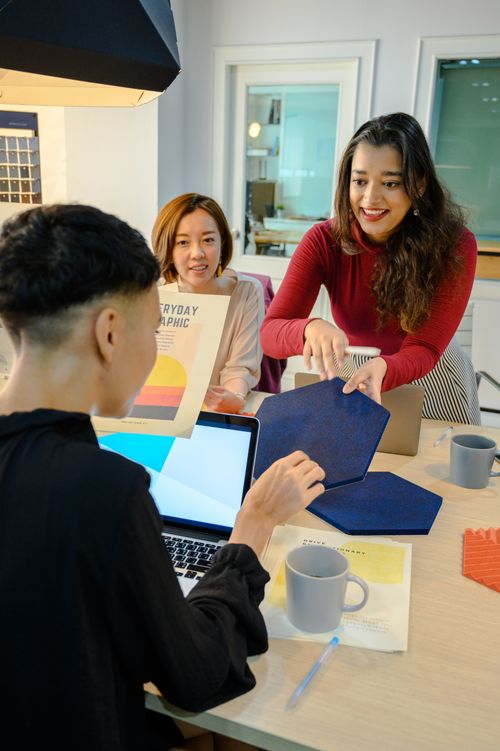Free Three colleagues discussing ideas around a desk with laptops, showcasing teamwork in a modern office environment. Stock Photo