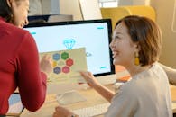 在现代办公环境中，两名女性正通过电脑屏幕讨论一份报告，以促进团队合作