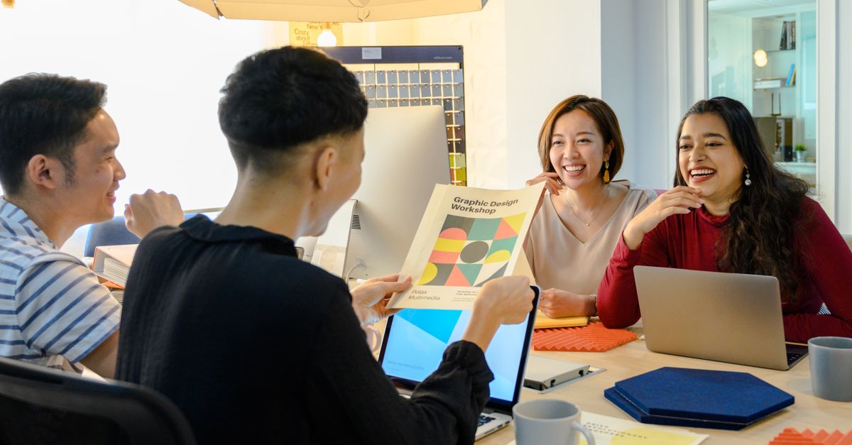 A diverse creative team in a lively meeting, discussing design ideas with laptops and a cheerful atmosphere.