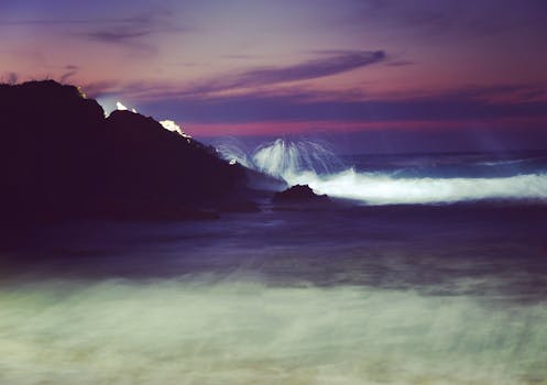Dramatic view of waves crashing on rocks during a colorful sunset in Greece.