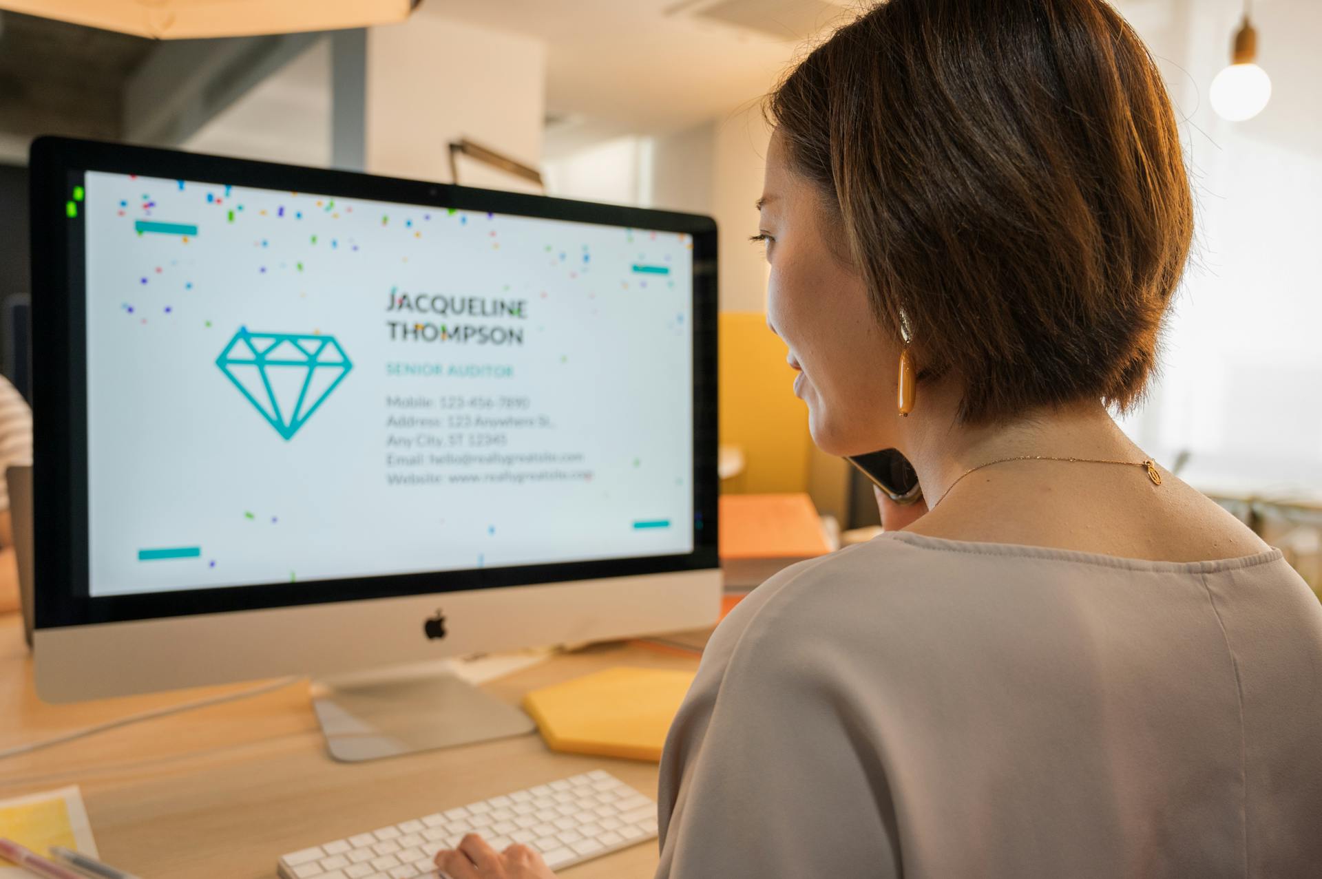 Businesswoman using a desktop computer in an office, viewing contact details on screen.