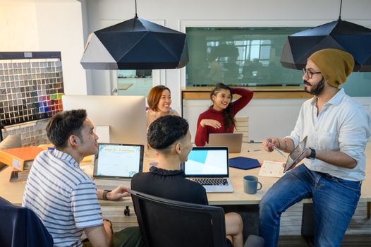 Diverse team discussing ideas around a table in a modern office with laptops and tablets.