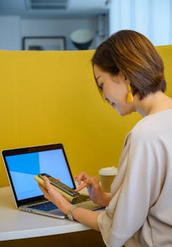 Woman multitasking with laptop and smartphone in a modern office setting.