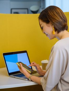 Woman using a smartphone while working on a laptop in a modern interior space.