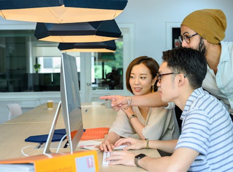 Three diverse adults collaborate on a computer project, discussing and pointing at the monitor.