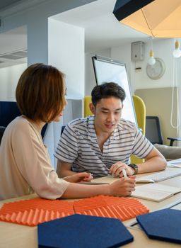两个成年人坐在木桌旁，用笔记本和笔合作讨论想法