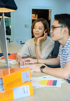 两位专业人士正坐在办公桌前，一起专注地看着电脑屏幕工作