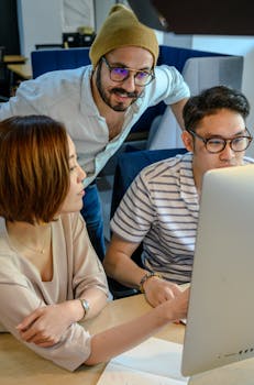 Diverse coworkers engaged in a collaborative discussion at an office desk around a computer.