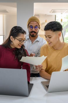 A group of diverse adults collaborating with laptops and papers in a modern office setting.