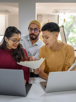 Young professionals engaging in a collaborative meeting using laptops and documents in a bright office.