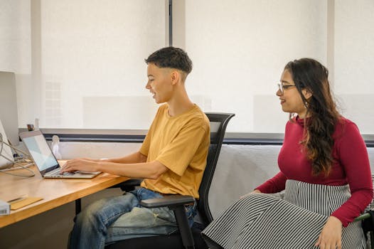 Two colleagues collaborate in a modern office setting with laptops, showcasing teamwork and diversity.