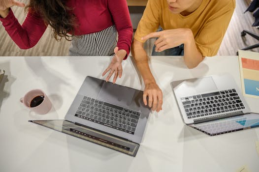 Two professionals engage in a collaborative discussion with laptops and coffee at a modern workspace.