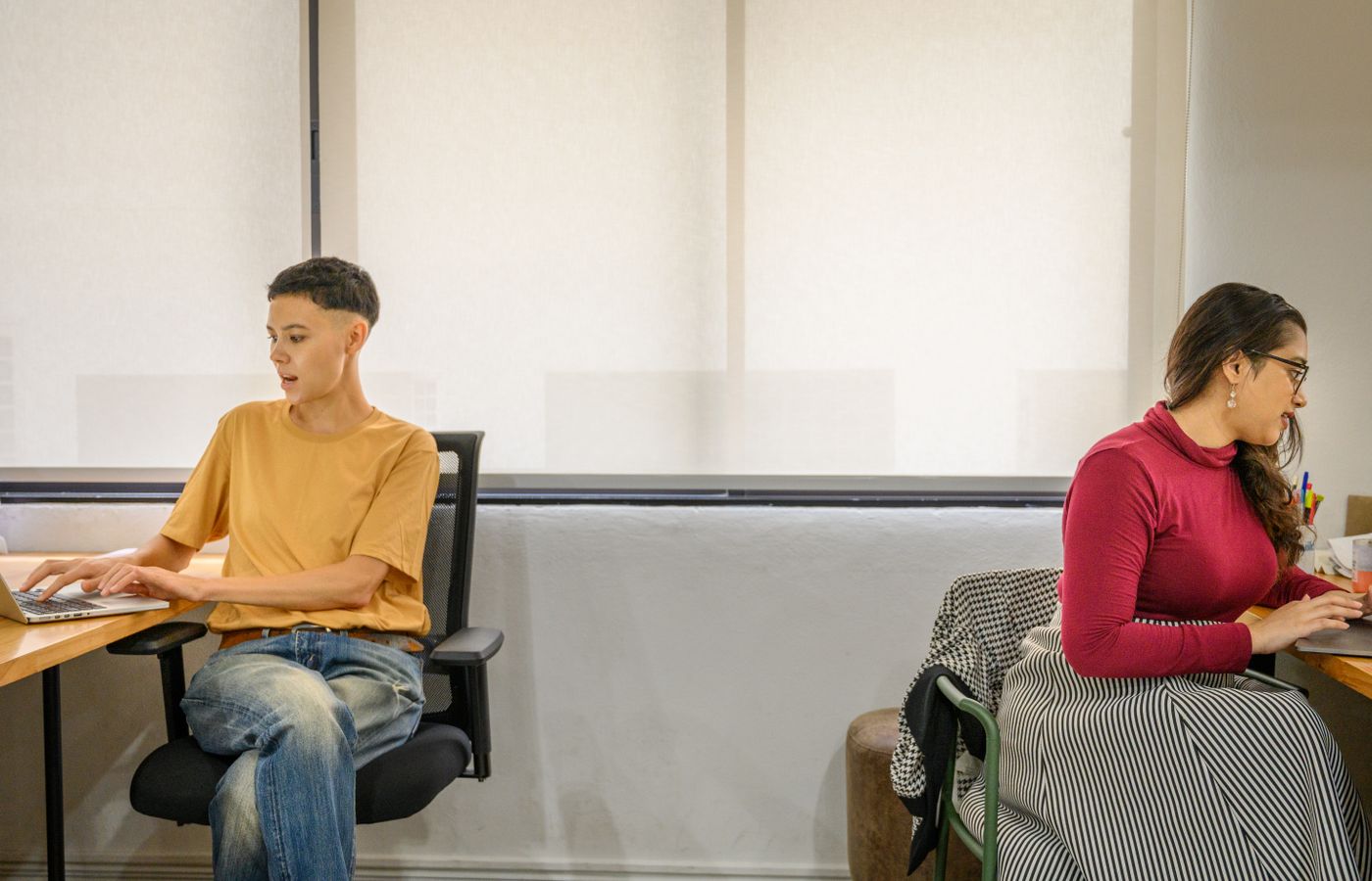 Two professionals working side by side at desks. Modern office setting with natural lighting.