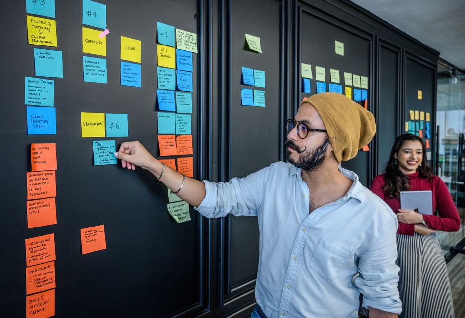 Two people organizing sticky notes on an office wall