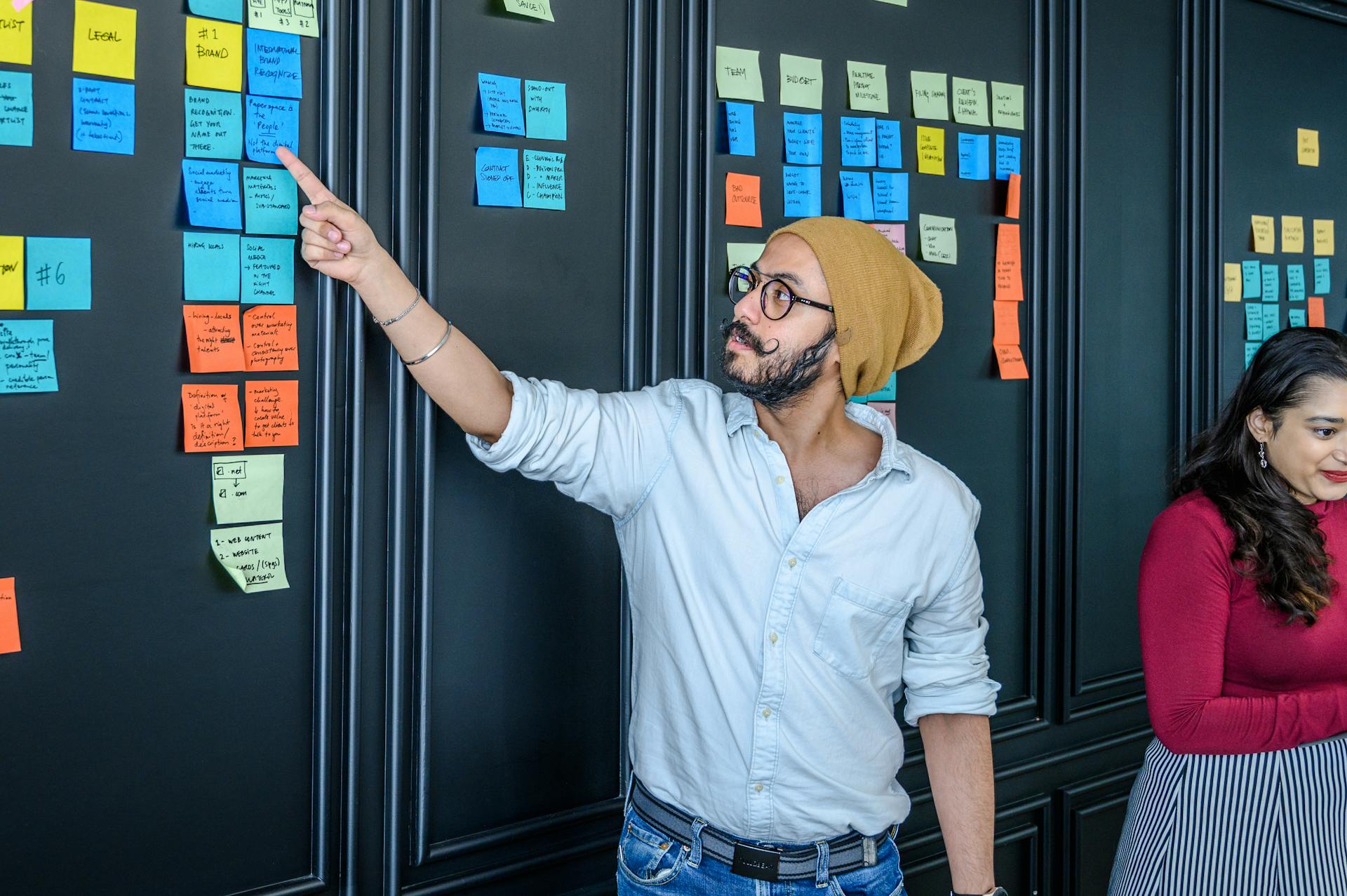 Man wearing beanie collaborates on project using sticky notes in office.