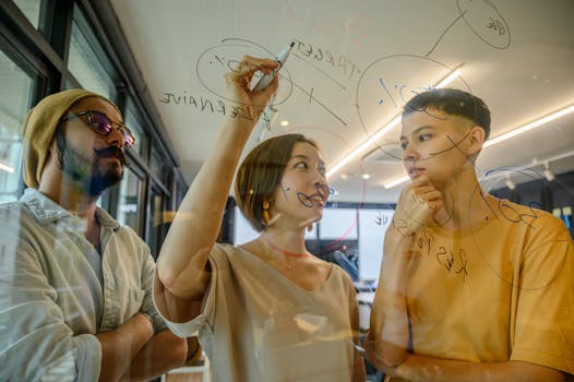 Three diverse young adults collaborating and brainstorming ideas on a glass board in a modern office setting.