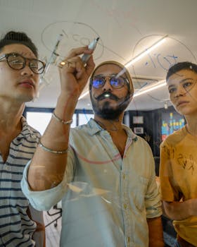 Three adults collaborate on ideas by writing on a glass panel during an office brainstorming session.