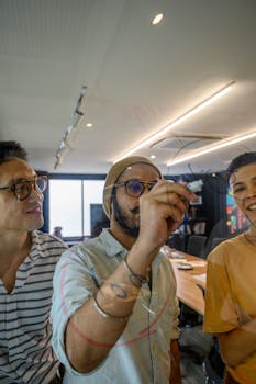 Three adults engaging in a collaborative discussion in a modern office, sketching ideas on a glass board.