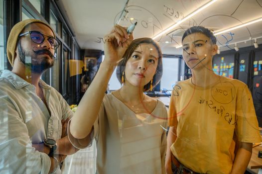 三名同事在现代办公室的玻璃上写下想法，参加了一次战略会议