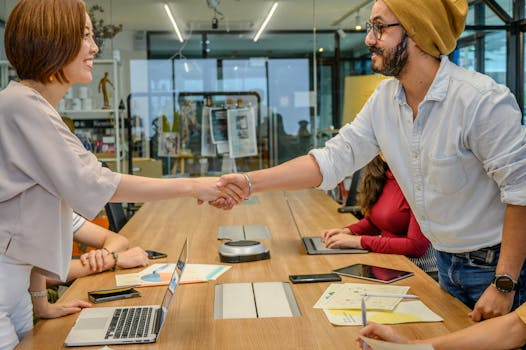 Diverse team in a modern office engaged in a collaborative meeting, sealing a partnership with a handshake.