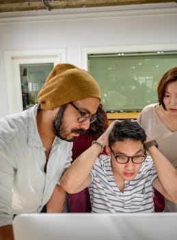 Three office workers react with surprise at a computer screen during a meeting.