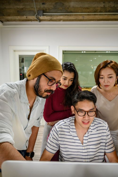 Free A diverse team collaborates around a computer in a contemporary office space. Stock Photo