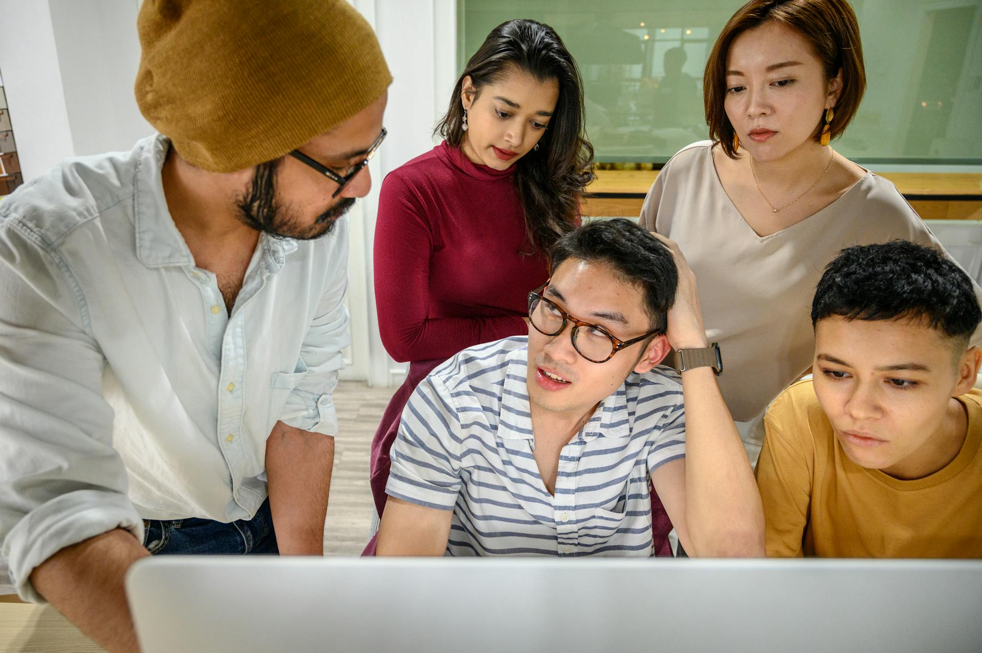 A diverse group of young professionals working together around a computer in a modern office setting.