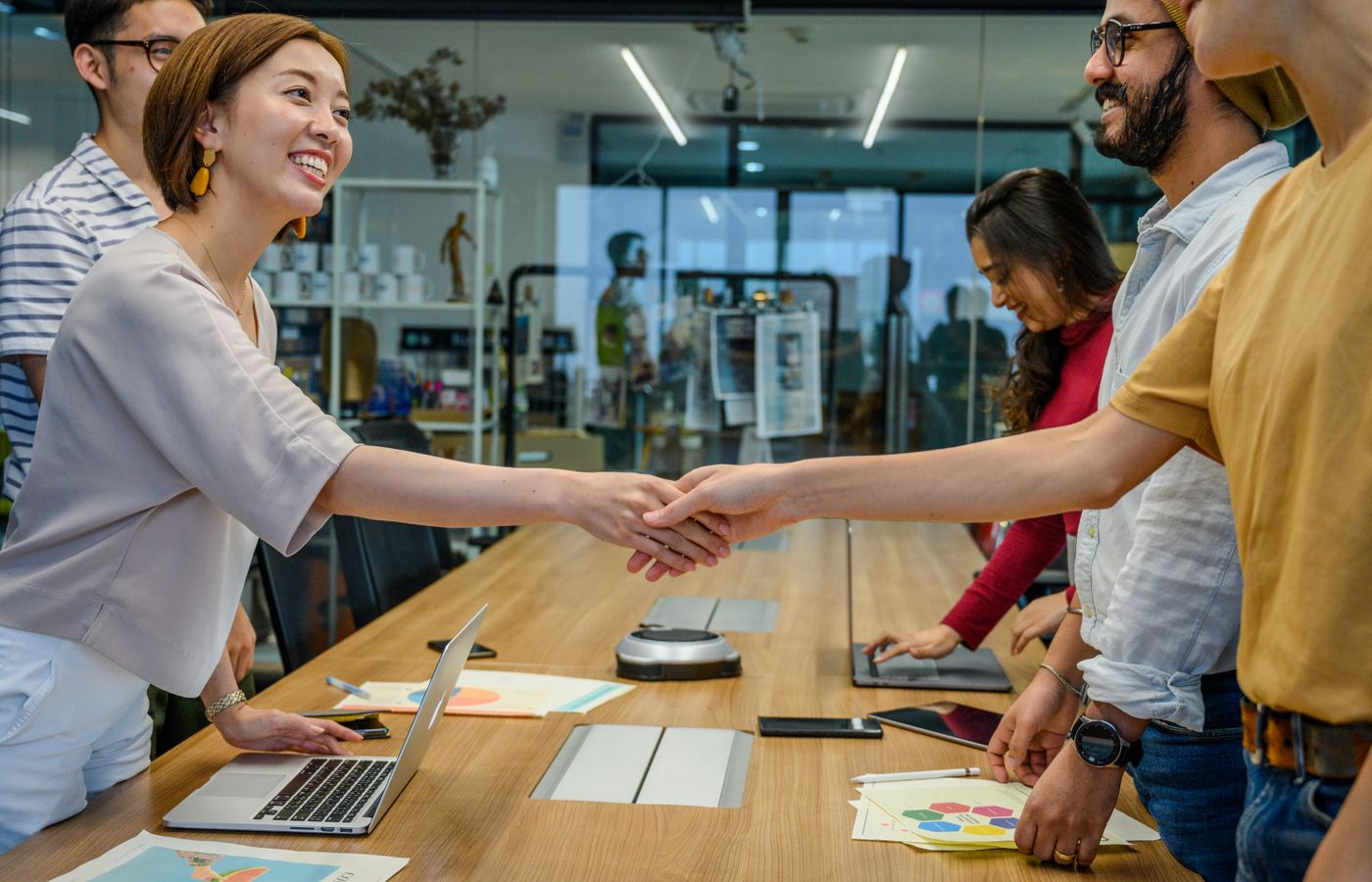 A diverse team of smiling professionals shaking hands during a productive meeting in a modern office.