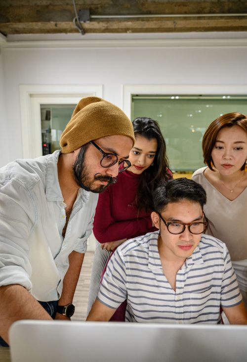 Free A diverse team of adults collaborating in a modern office, focused on a computer screen. Stock Photo