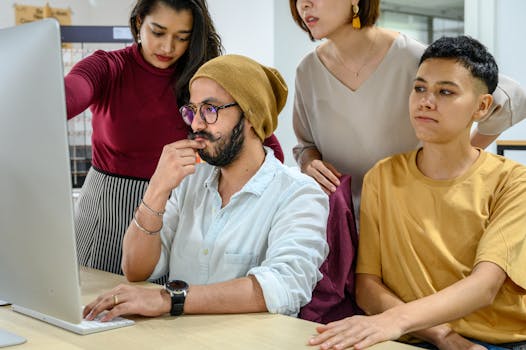 Diverse colleagues collaborating at a computer in a modern office setting.